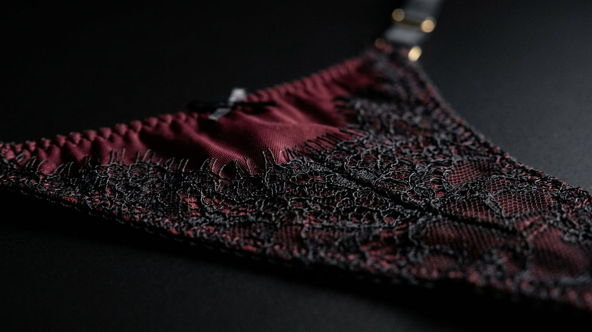 Extreme close-up of hand-finished lace edging and visible stitch detail on a burgundy mesh panel