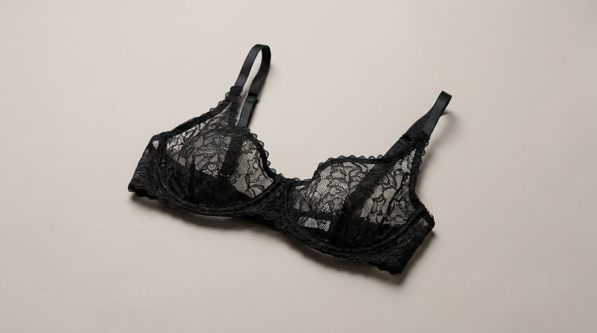 A black lace underwire bra with adjustable shoulder straps, laid flat on a light beige background.