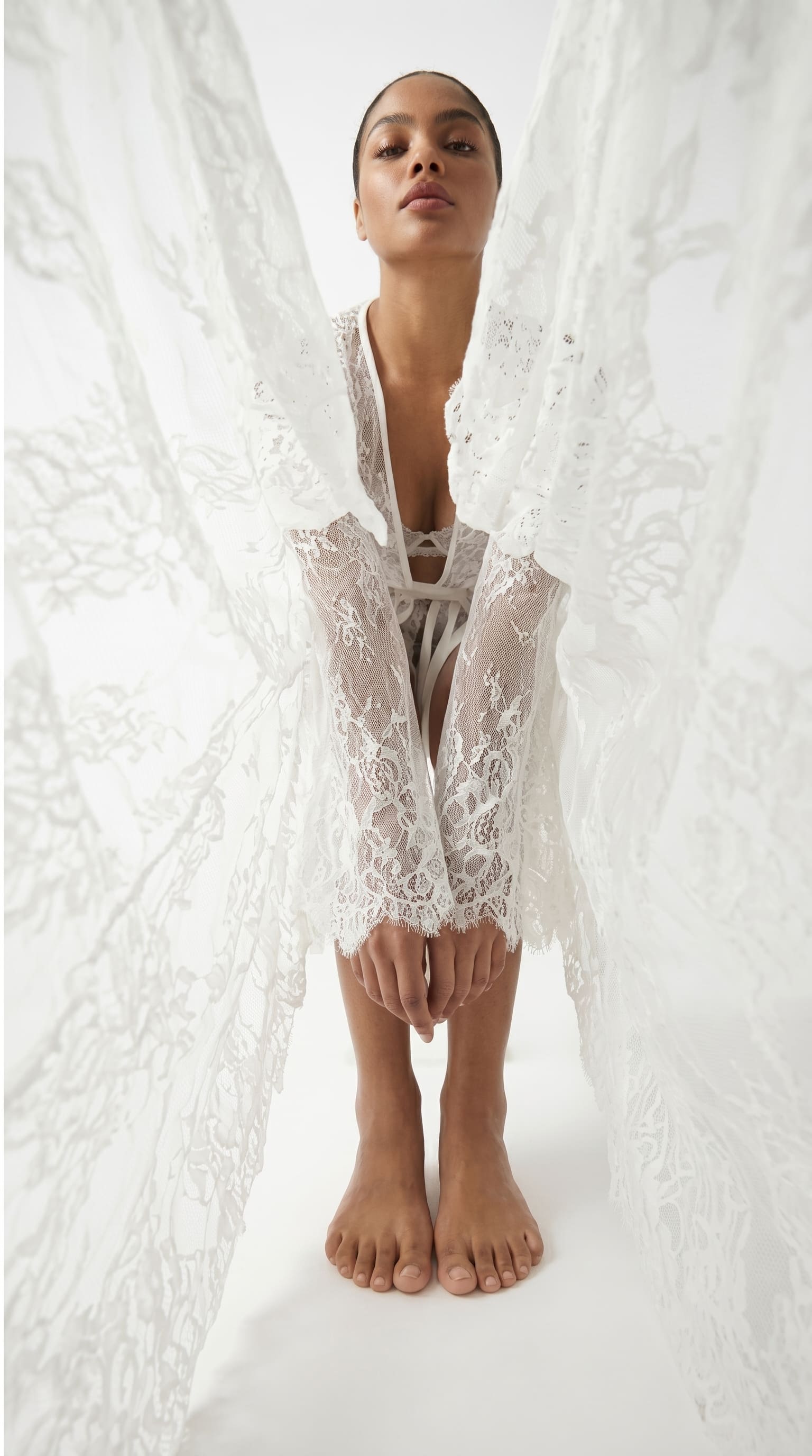 Front view of a white sheer lace robe, styled amid flowing lace drapery.